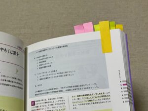 紙の技術書に貼られた大量の付箋。物理的な検索性とアクセス速度(ゼロ・レイテンシ)を象徴するアナログの強み。