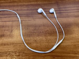 木のデスクの上に置かれた、AI音声入力用の白いマイク付き有線イヤホンの写真。