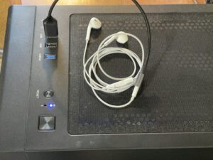 デスクトップパソコンのUSBポートに接続された、AI音声入力用の白い有線イヤホンマイクの写真。